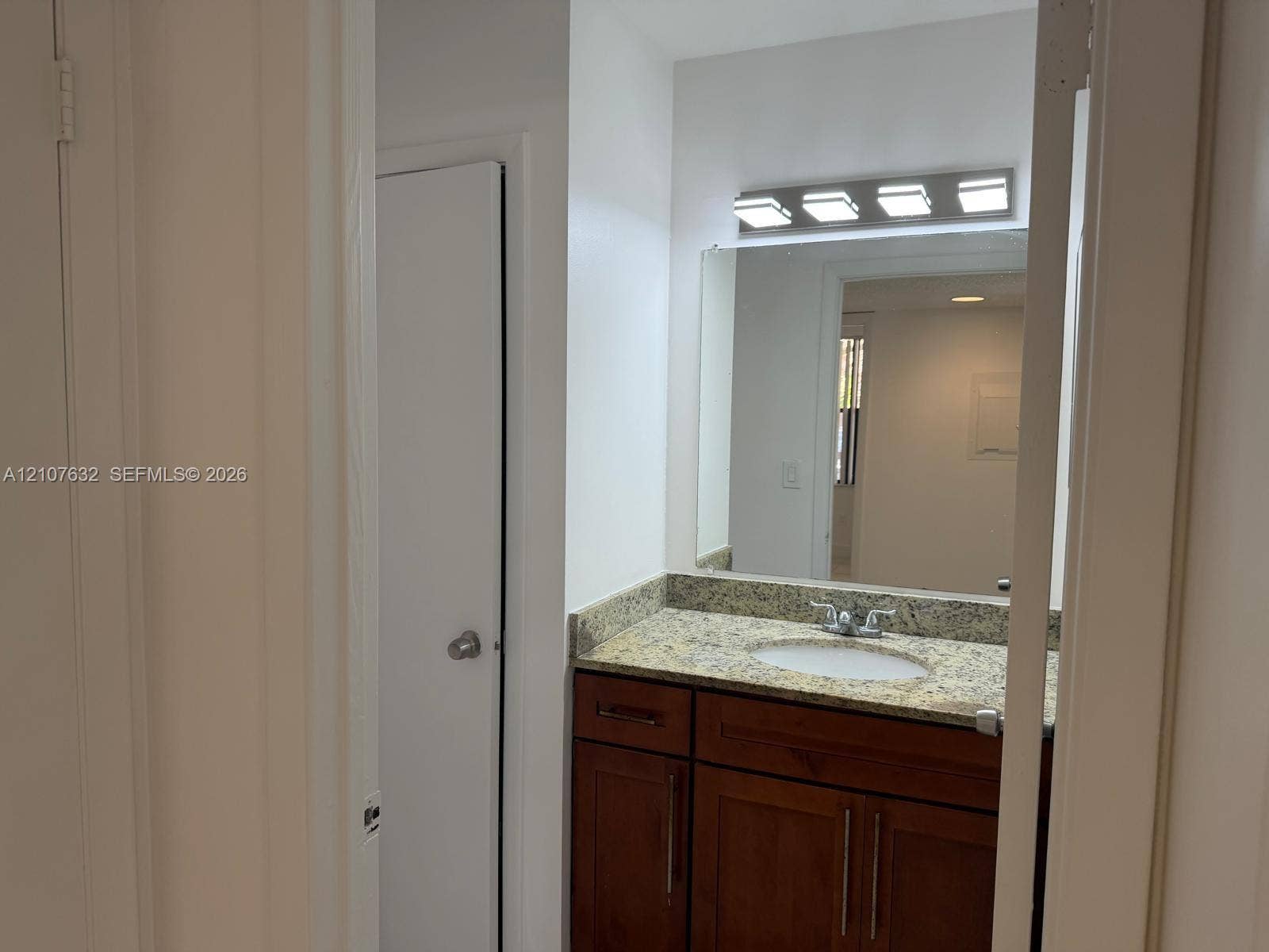4501 W Mcnab Road, #13, Pompano Beach, Pompano Beach, FL 33069 Vanity featuring a dark wood-finish cabinet, stone-finish countertop with an undermount oval sink, chrome dual-handle faucet, full-width mirror, and four-light overhead fixture