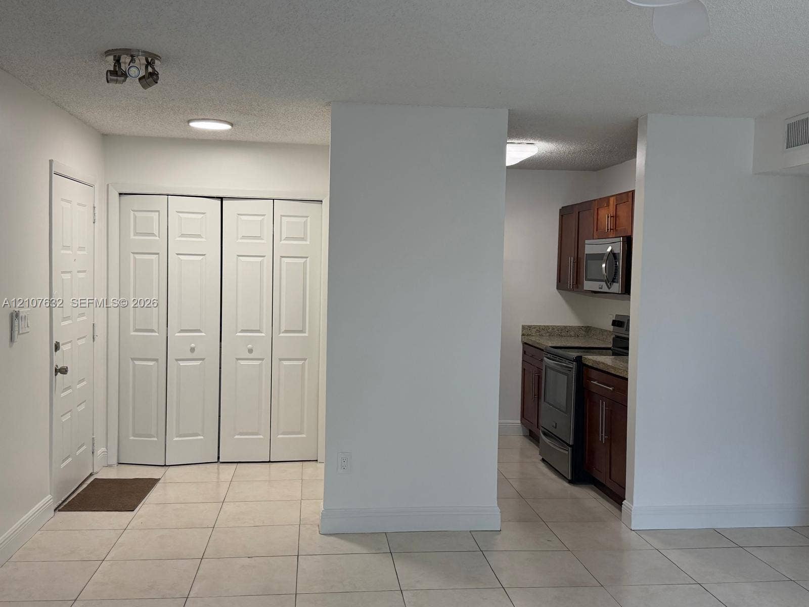 4501 W Mcnab Road, #13, Pompano Beach, Pompano Beach, FL 33069 Kitchen area featuring wood-finish cabinetry, stone-style countertops, and stainless steel appliances, complemented by light-toned tile flooring and double-panel closet doors