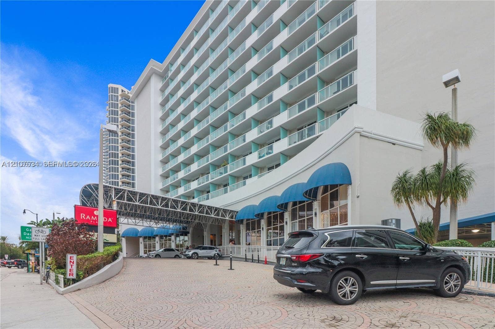 19201 Collins Avenue, #941, Sunny Isles Beach, FL 33160 High-rise exterior featuring stacked cantilevered balconies, decorative blue fabric awnings, a paved circular drive, and multi-story glass-paned ground level frontage