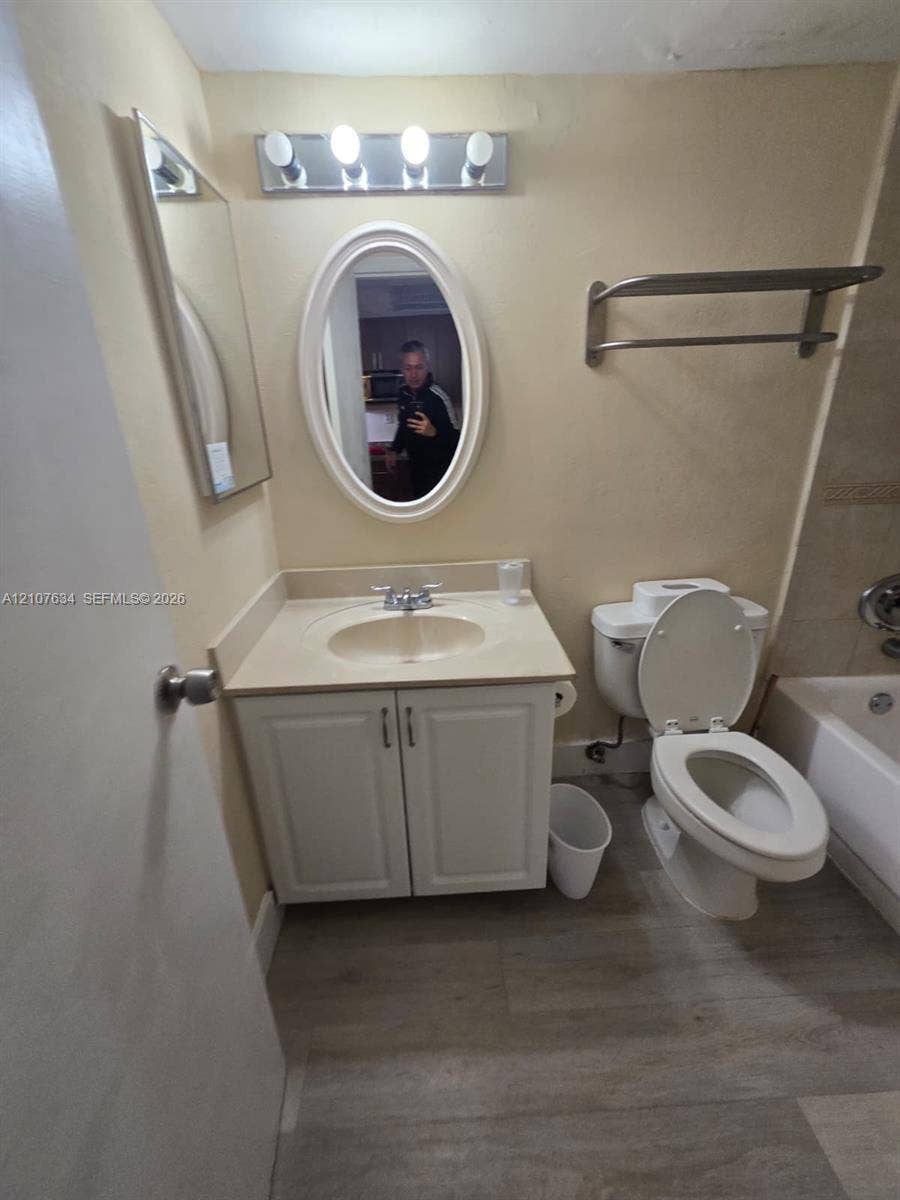 19201 Collins Avenue, #941, Sunny Isles Beach, FL 33160 Bathroom vanity with a white cabinet, integrated countertop, and oval-shaped wall mirror, complemented by wood-finish flooring, a wall-mounted towel rack, and four-bulb vanity lighting