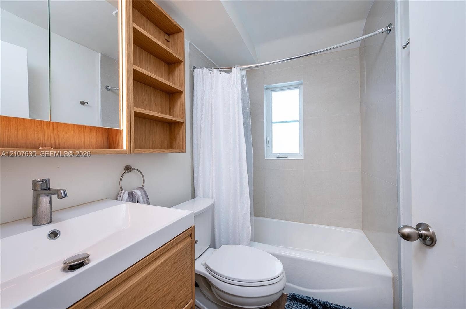 217 Madeira Avenue, #3, Coral Gables, Coral Gables, FL 33134 Wood-finish vanity with integrated rectangular sink and side shelving, wall-mounted lighted medicine cabinet, and combination tub and shower with light-toned wall tile