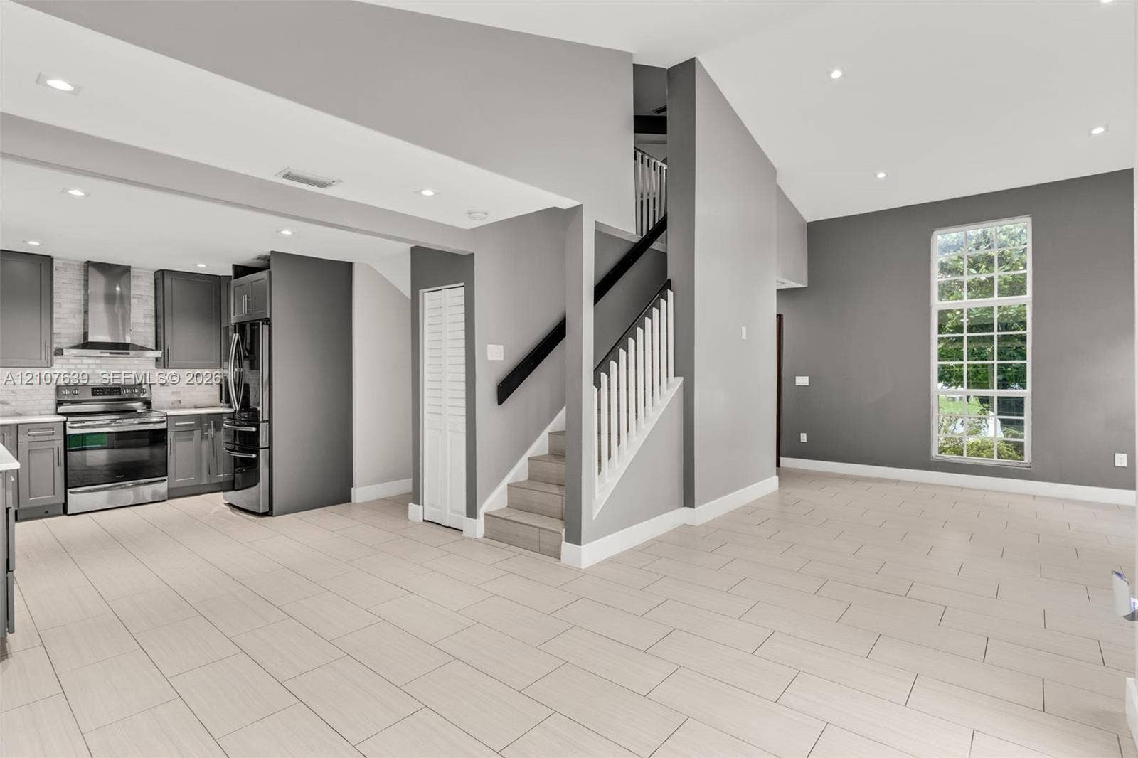 11735 SW 114th Terrace, #11735, Miami, Miami, FL 33186 Open-concept interior featuring vaulted ceilings, recessed lighting, tile flooring, a staircase with a white spindle railing, and a kitchen equipped with stainless steel appliances and custom cabinetry