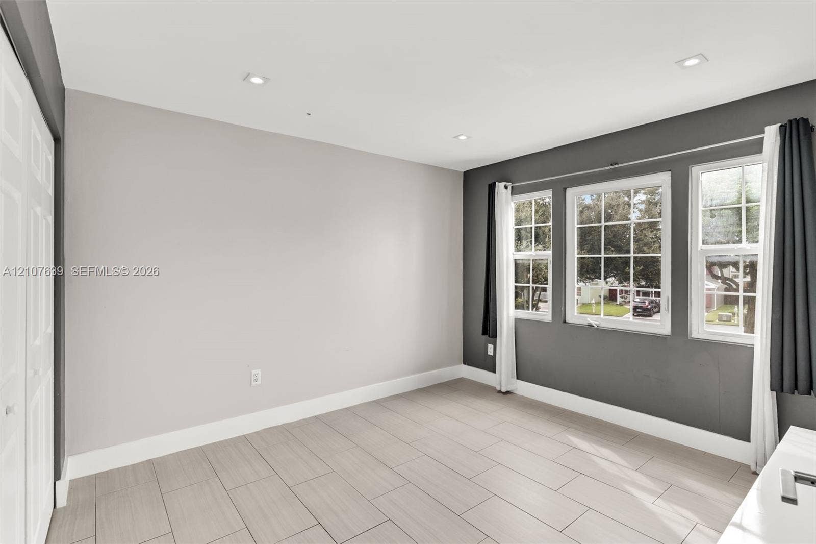 11735 SW 114th Terrace, #11735, Miami, Miami, FL 33186 Neutral-toned room featuring large-format tile flooring, recessed ceiling lighting, three divided-light windows, and bi-fold closet doors