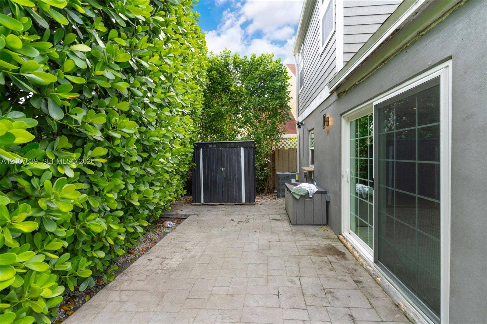 11735 SW 114th Terrace, #11735, Miami, Miami, FL 33186 Side patio featuring paved hardscaping, a full-height privacy hedge, and sliding glass door entry