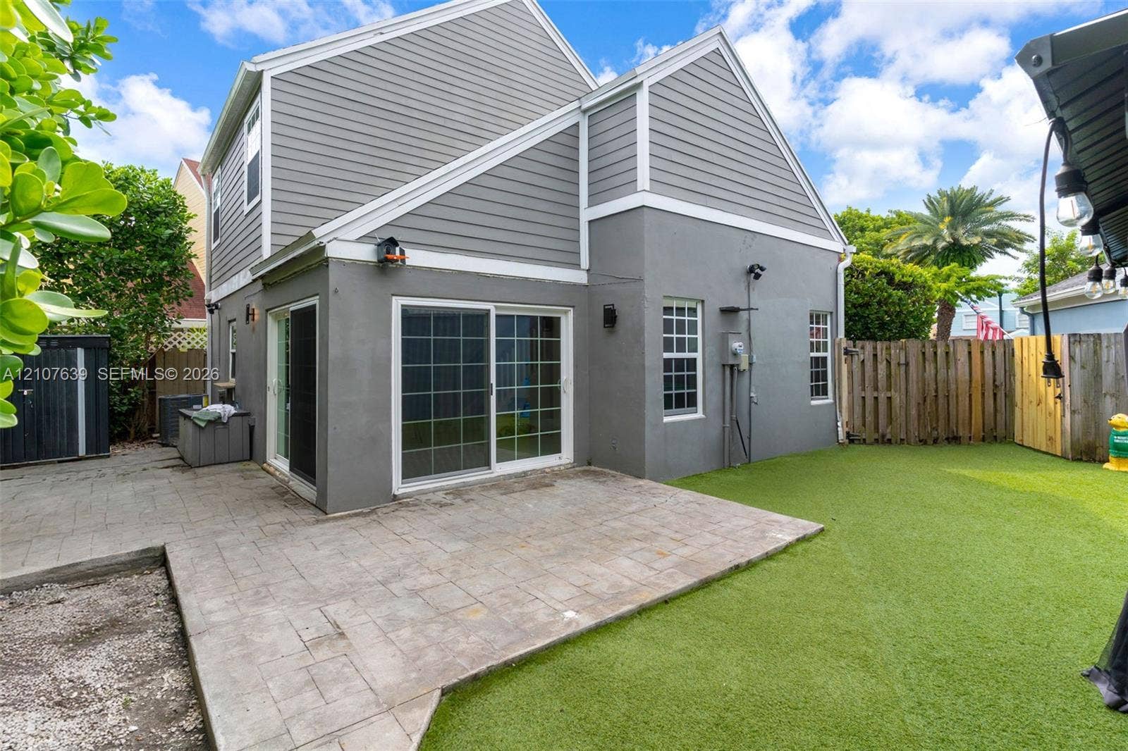 11735 SW 114th Terrace, #11735, Miami, Miami, FL 33186 Exterior featuring grey horizontal siding and smooth-finish stucco, paver patio, sliding glass doors, and artificial turf lawn enclosed by wood fencing