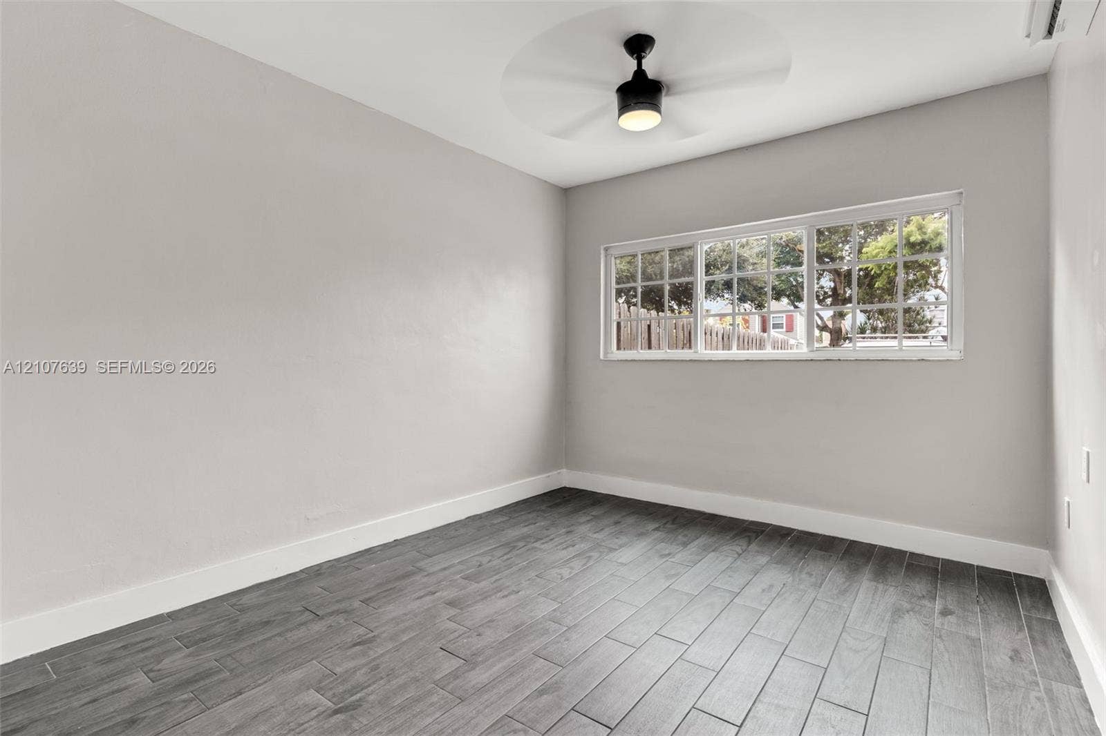 11735 SW 114th Terrace, #11735, Miami, Miami, FL 33186 Room interior featuring grey wood-finish flooring, neutral wall paint, a multi-pane horizontal window, and a ceiling-mounted light fixture with a fan