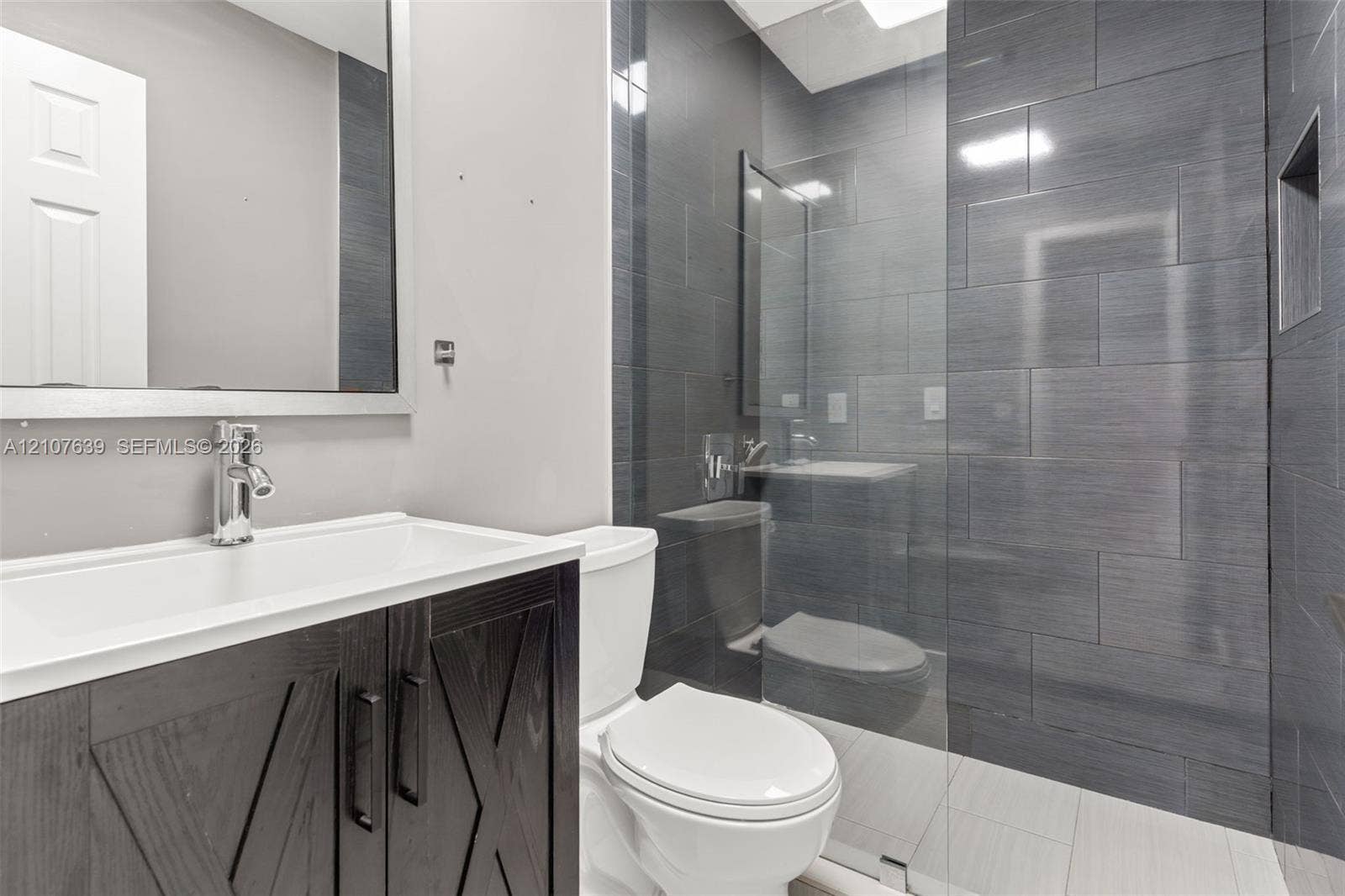 11735 SW 114th Terrace, #11735, Miami, Miami, FL 33186 Bathroom featuring a vanity with dark wood-finish cabinetry, a glass-enclosed shower with charcoal-toned tile surround, built-in shower niche, and rectangular wall mirror