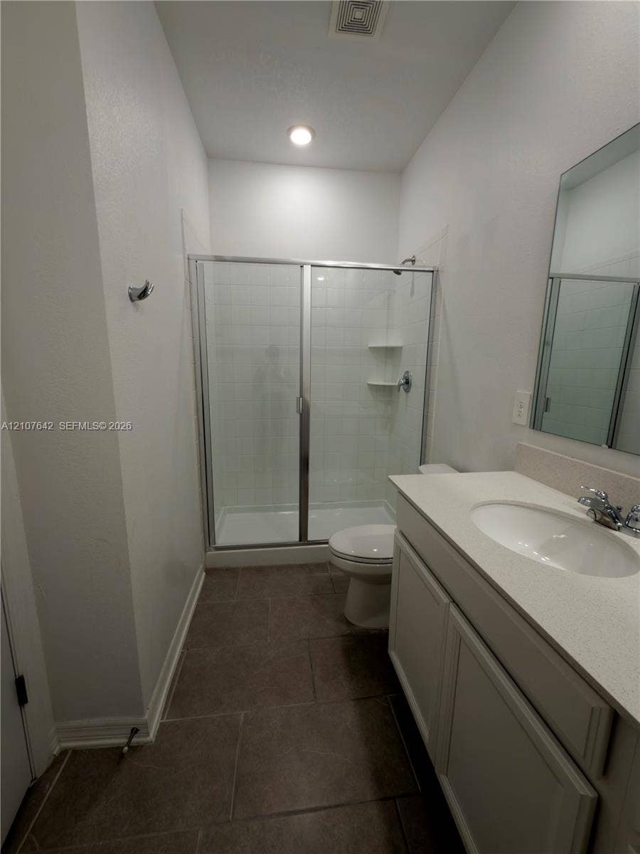 664 Tanaro Lane, Haines City, FL 33844 Bathroom featuring a glass-enclosed shower with tiled surround, stone-composite countertop with integrated sink, white cabinetry, and ceramic tile flooring