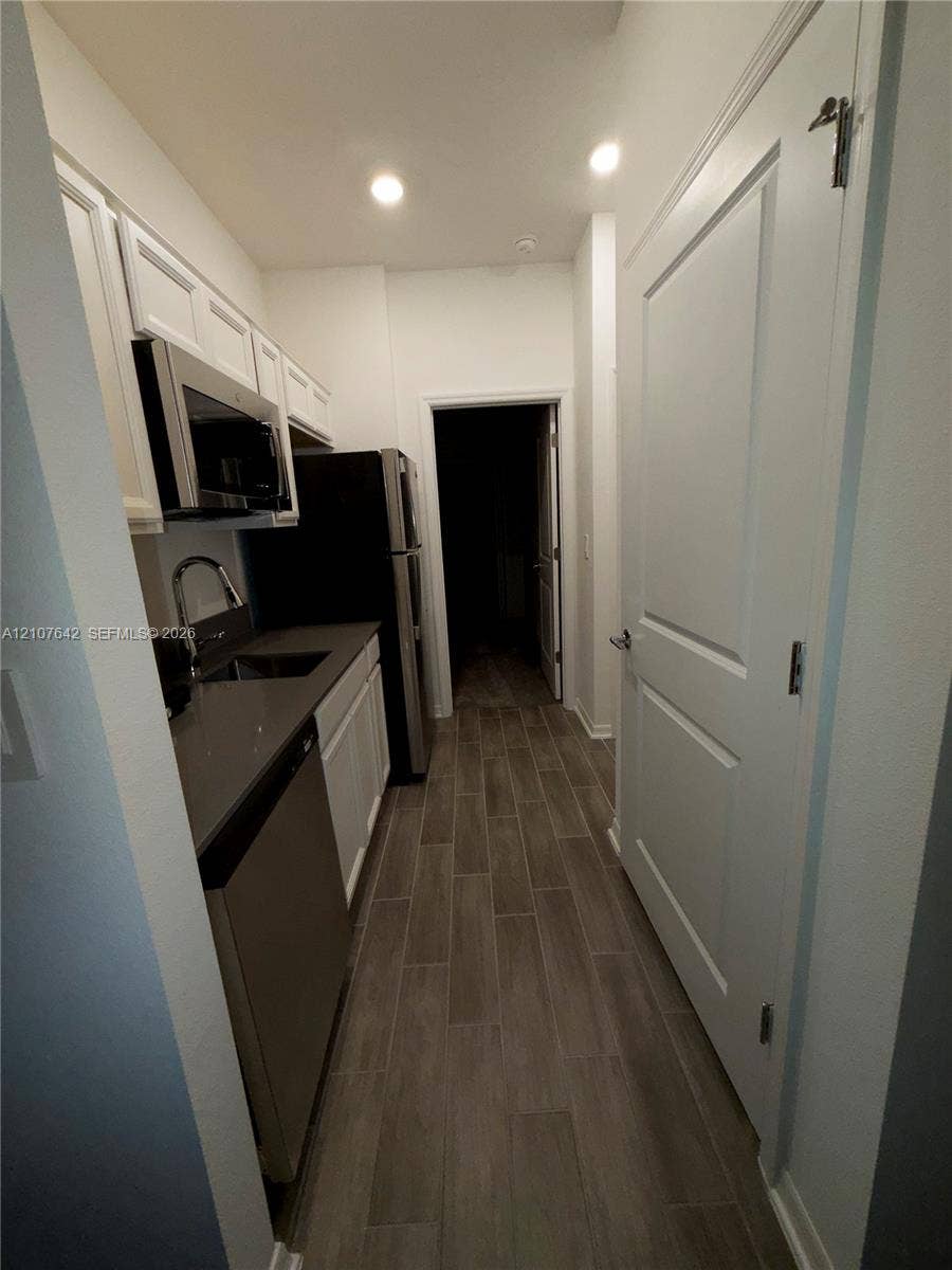 664 Tanaro Lane, Haines City, FL 33844 Kitchen featuring white shaker-style cabinetry, solid-surface countertops, wood-finish tile flooring, recessed ceiling lighting, and stainless steel appliances