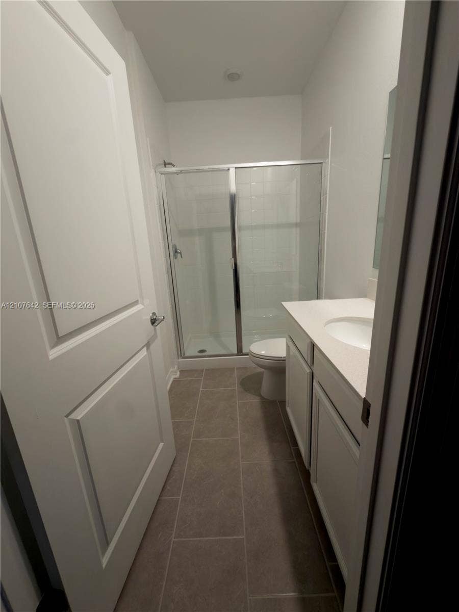 664 Tanaro Lane, Haines City, FL 33844 Bathroom featuring tile flooring, a white vanity with a composite countertop, a glass-enclosed shower, and a two-panel interior door