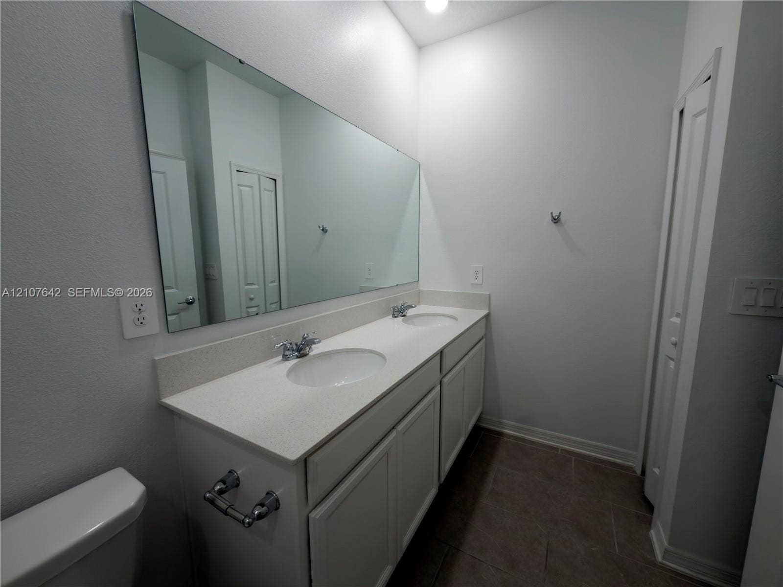 664 Tanaro Lane, Haines City, FL 33844 Dual-sink vanity with a solid-surface countertop, white cabinetry, integrated oval basins, chrome fixtures, and a wall-to-wall mirror