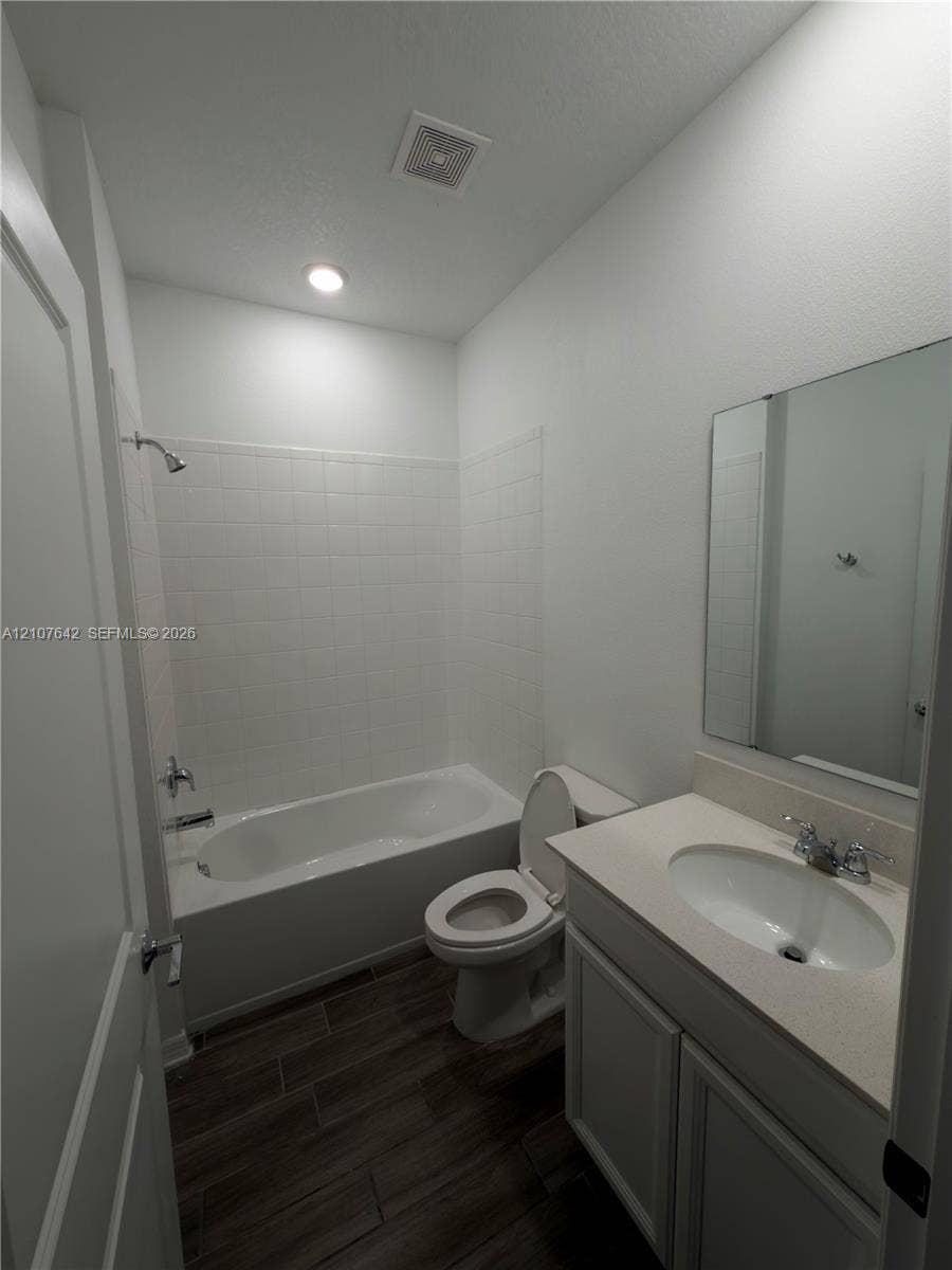 664 Tanaro Lane, Haines City, FL 33844 Bathroom featuring wood-finish tile flooring, a single-sink vanity with a solid-surface countertop, and a shower-tub combination with a tiled surround