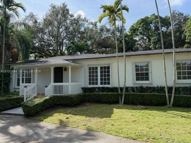 7550 SW 67th Avenue, South Miami, South Miami, FL 33143 Single-story residence featuring a smooth stucco exterior, covered front porch with white railing, grid-pattern windows, and asphalt shingle roofing