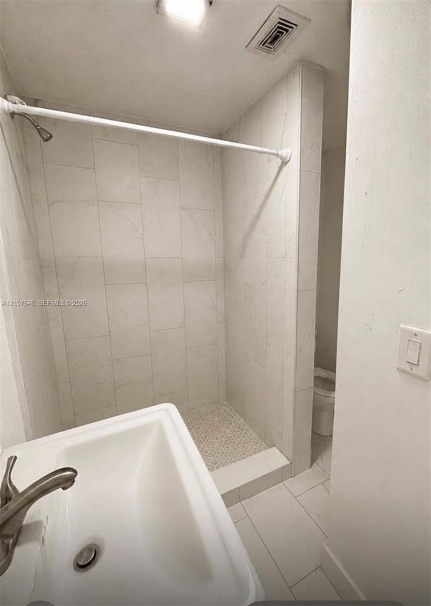 75 NW 116th Street, Miami, FL 33168 Shower featuring floor-to-ceiling large-format tile surround, mosaic tile flooring, and a wall-mounted sink with a metallic finish faucet