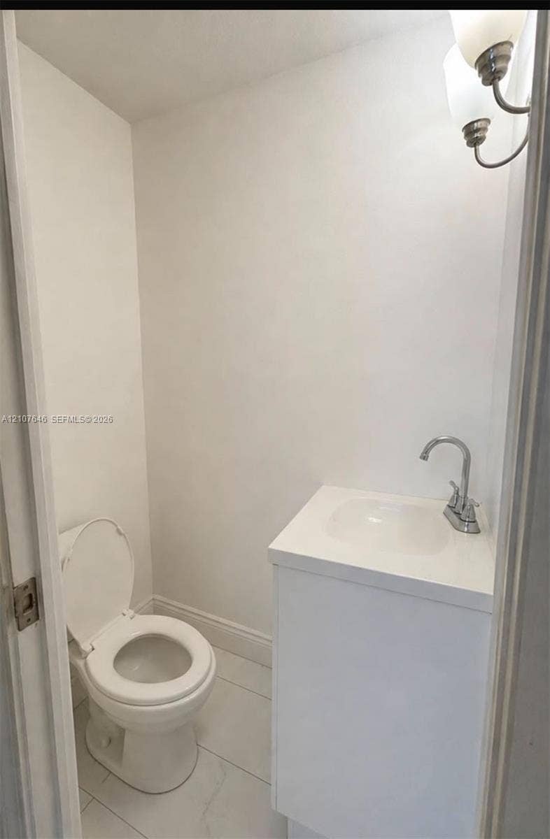 75 NW 116th Street, Miami, FL 33168 Compact powder room featuring large-format tile flooring, a white vanity with an integrated countertop basin, and a dual-bulb wall-mounted light fixture
