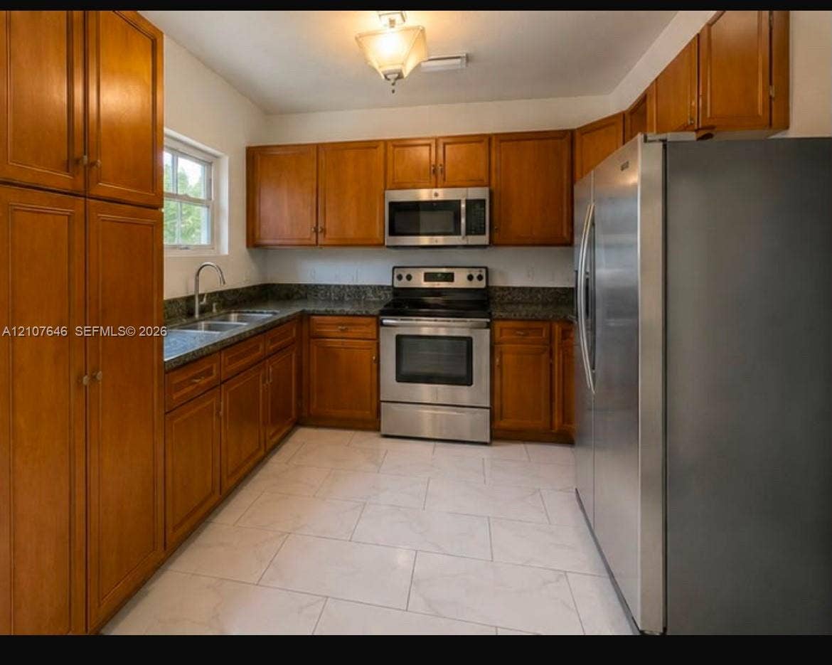75 NW 116th Street, Miami, FL 33168 Kitchen featuring wood cabinetry, stone-surface countertops, stainless steel appliances, and large-format tile flooring