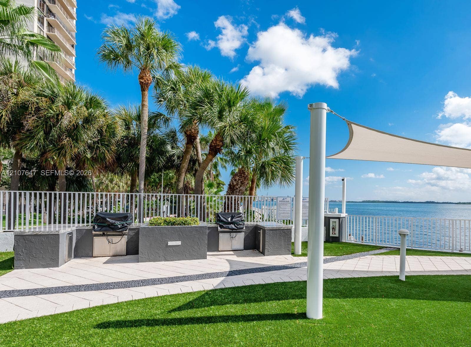 200 SE 15th Road, #PH-A, Miami, Miami, FL 33129 Outdoor cooking area featuring stone-finish counters, built-in stainless steel grills, artificial turf lawn, decorative paver walkway, and a tension shade structure overlooking the water