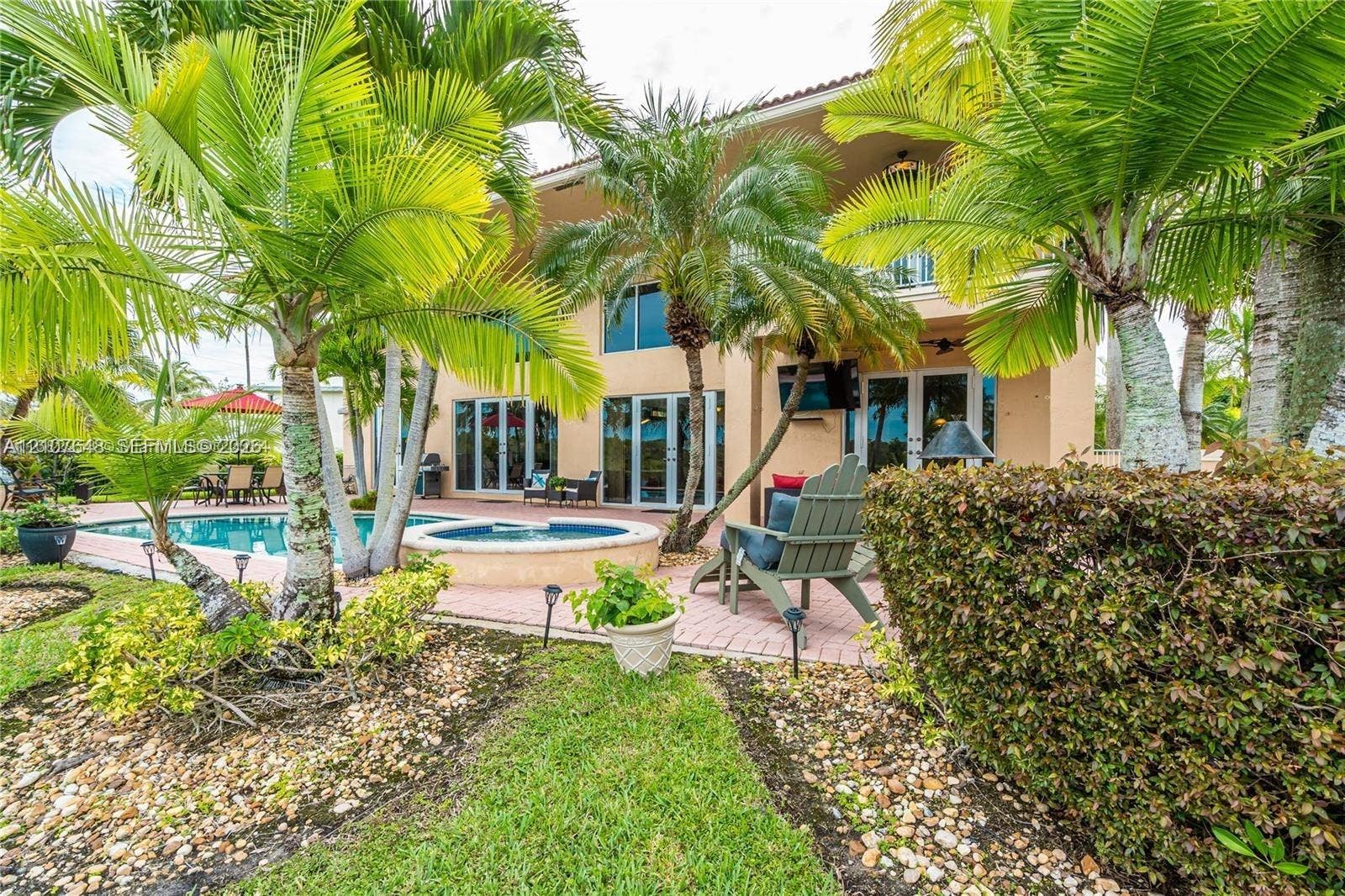 Two-story exterior featuring a brick-paver patio, a swimming pool with an integrated spa, and mature palm landscaping