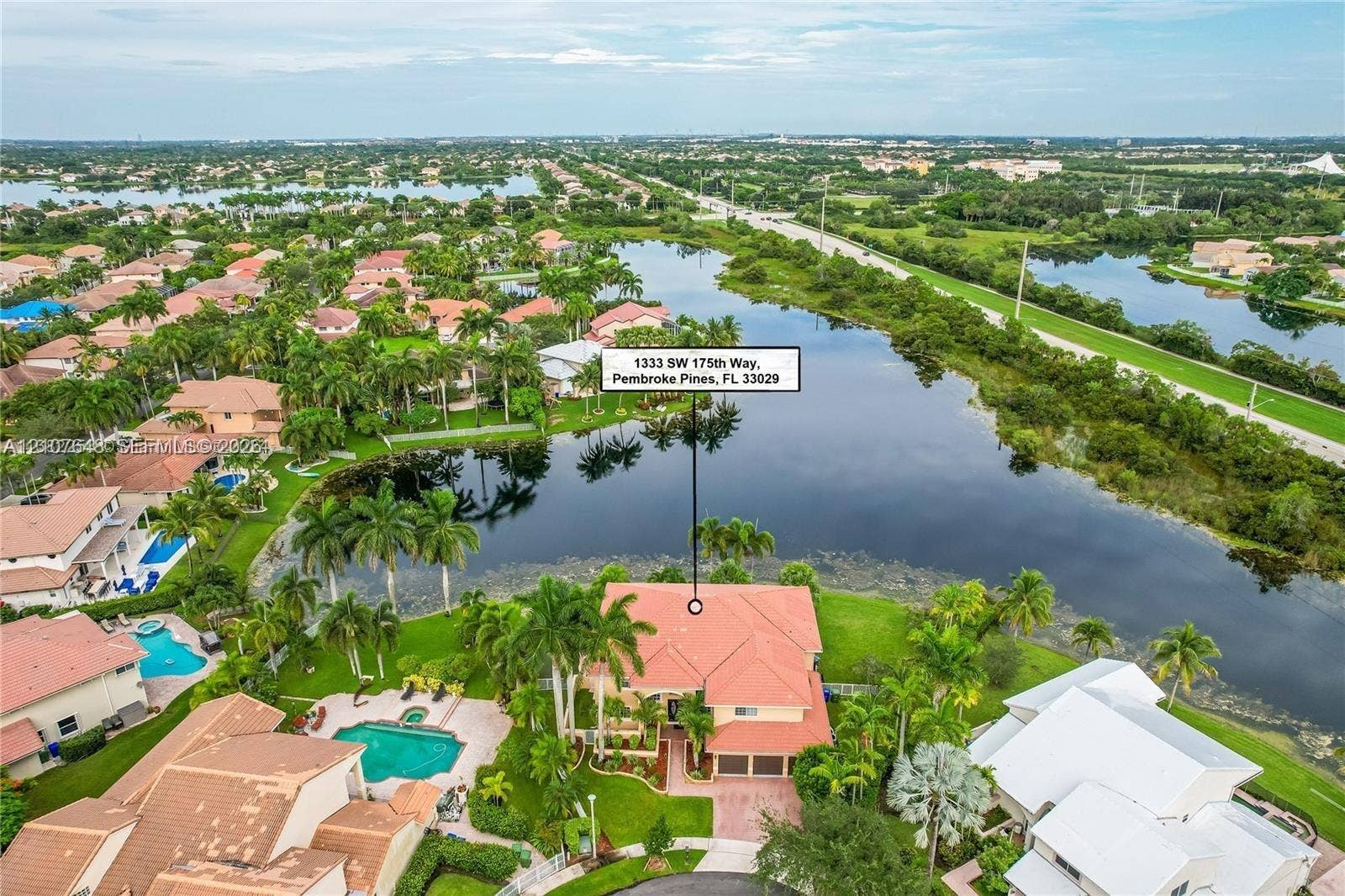 Aerial perspective of waterfront property featuring a tile roof, paved driveway, two-car garage, and established landscaping