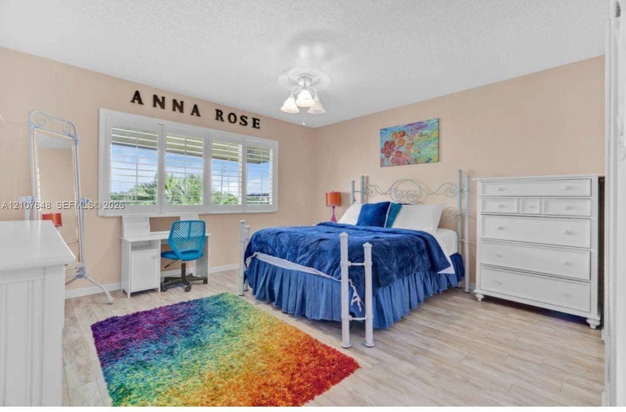 Bedroom featuring wood-finish flooring, plantation shutters, and a multi-globe ceiling-mounted light fixture