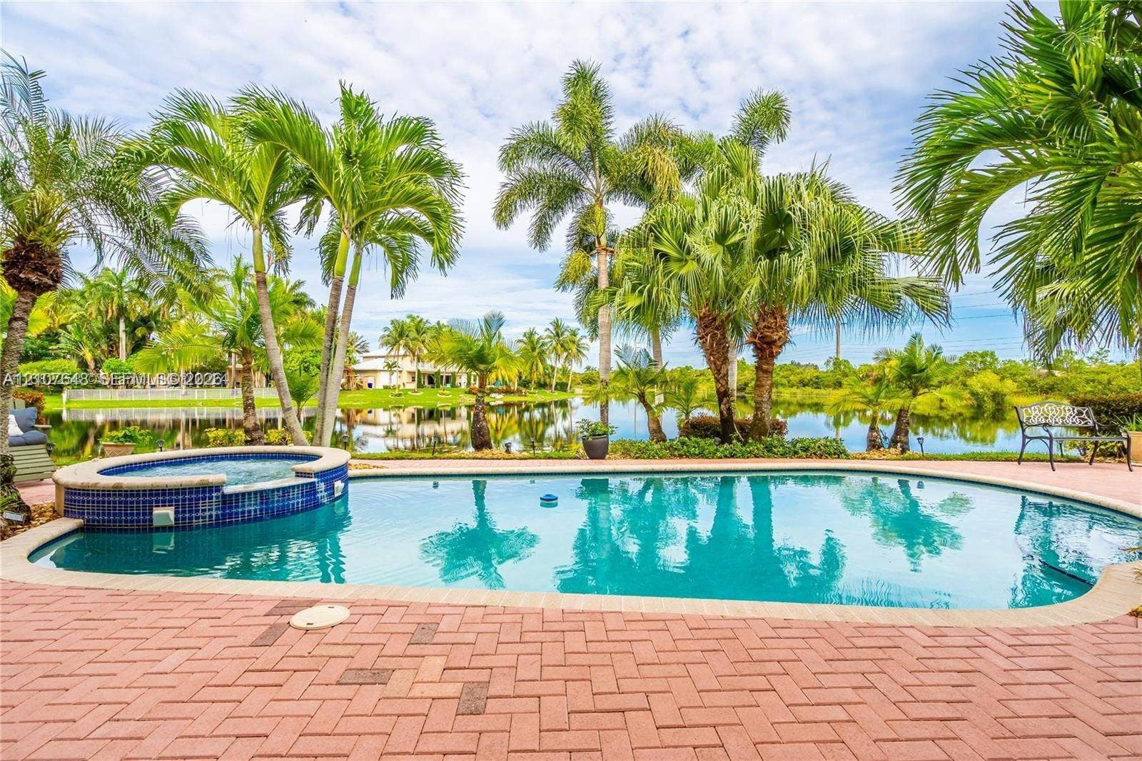 In-ground pool featuring a raised spa, blue glass-tile spillover, brick paver patio, and water frontage with mature palm trees