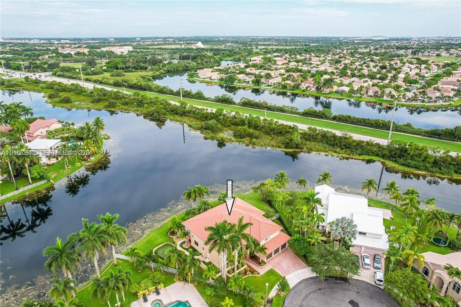 Waterfront residence featuring a tiled roof, multi-car garage, paved driveway, and mature landscaping situated along a canal
