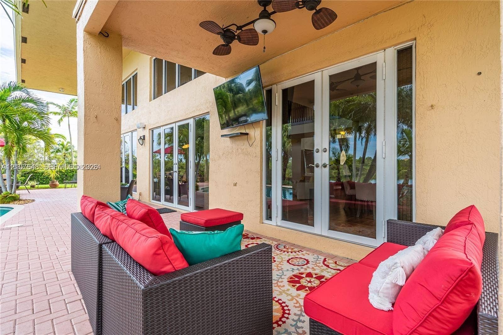 Covered patio featuring paver flooring, stucco wall finish, wall-mounted television, and dual sets of glass French doors