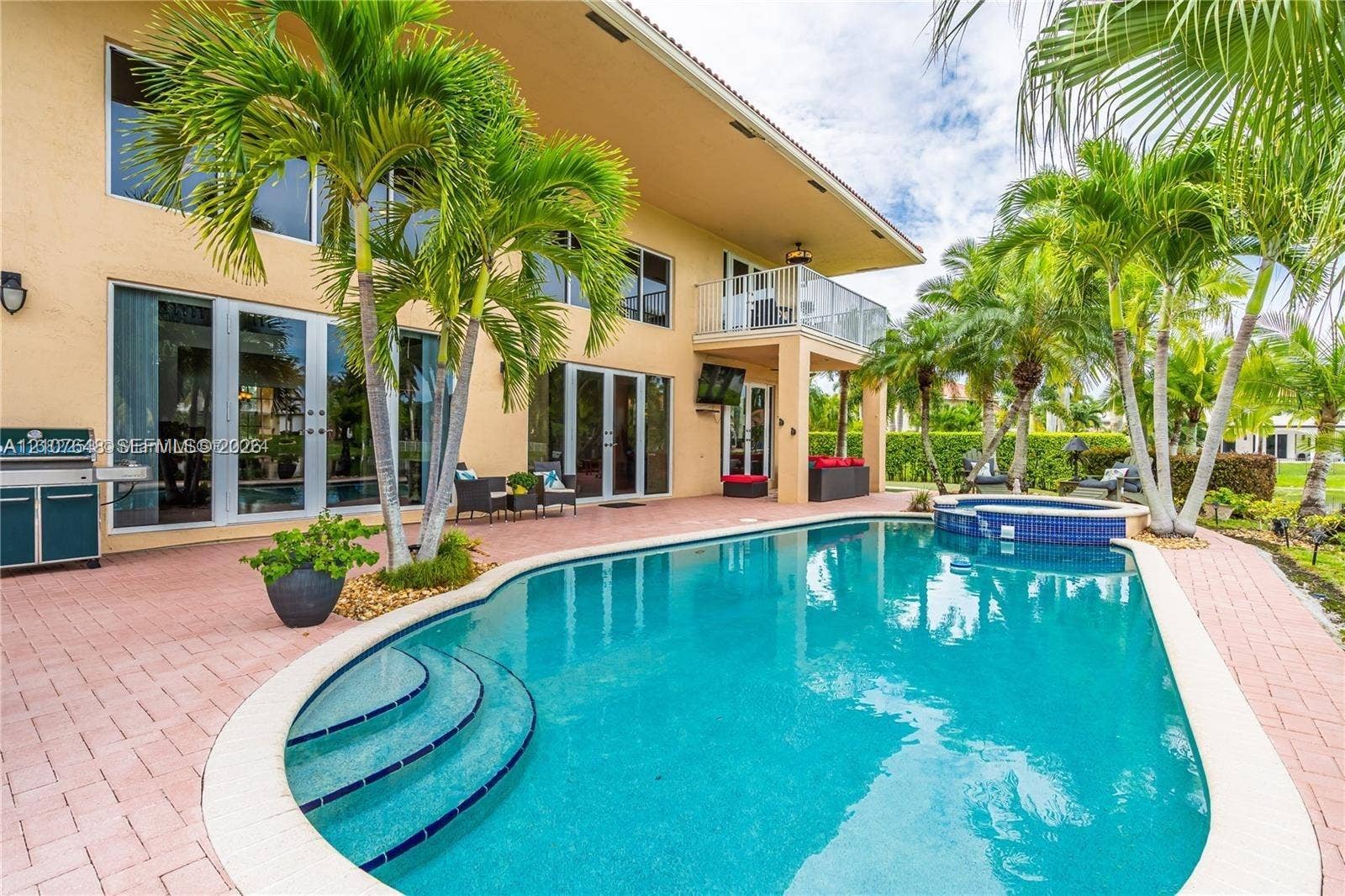 In-ground pool with integrated spa, paver patio, second-story balcony with metal railing, and built-in stainless steel outdoor kitchen station
