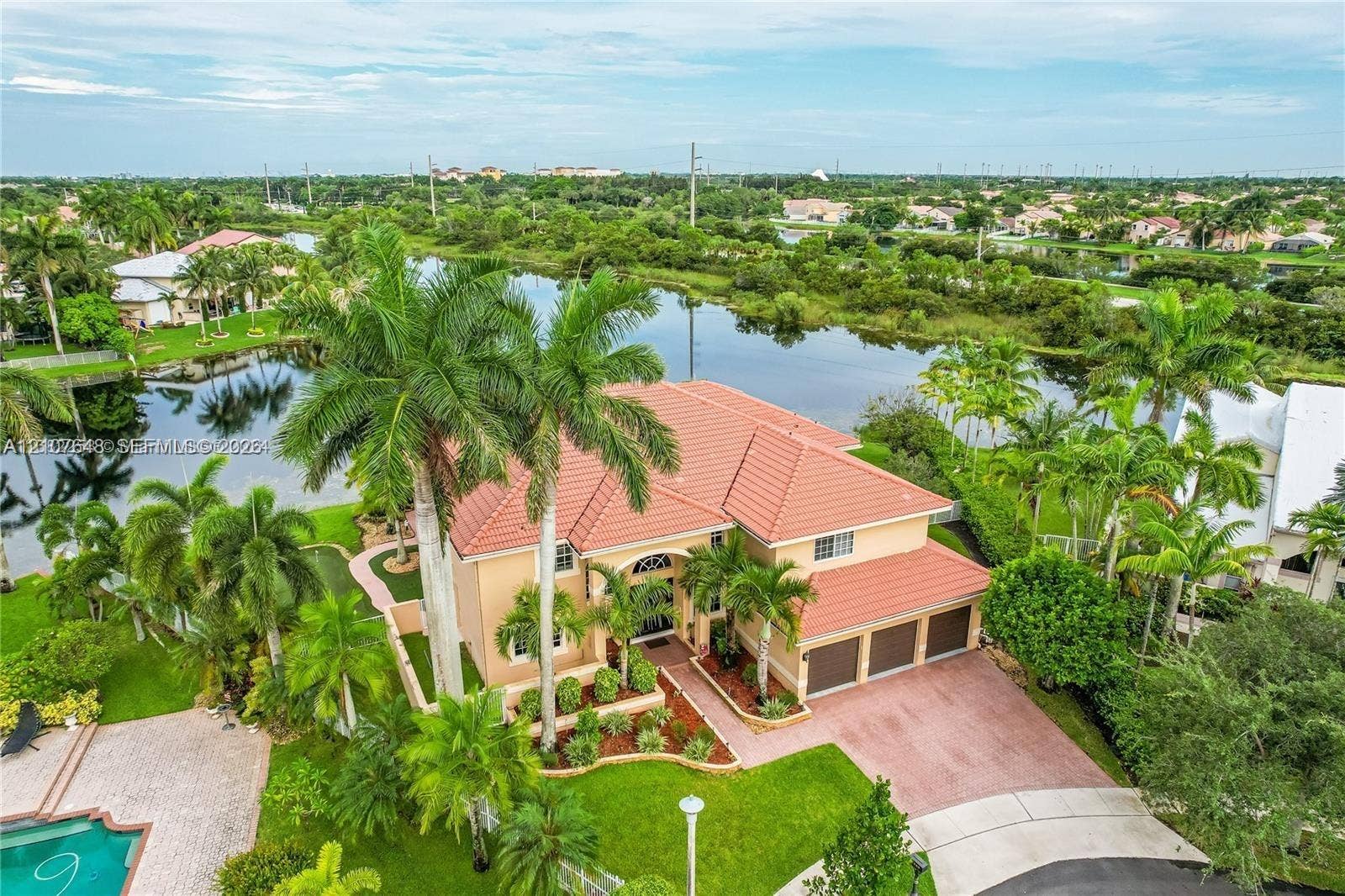 Two-story residence featuring a tile roof, three-car garage, paver driveway, swimming pool, and water frontage