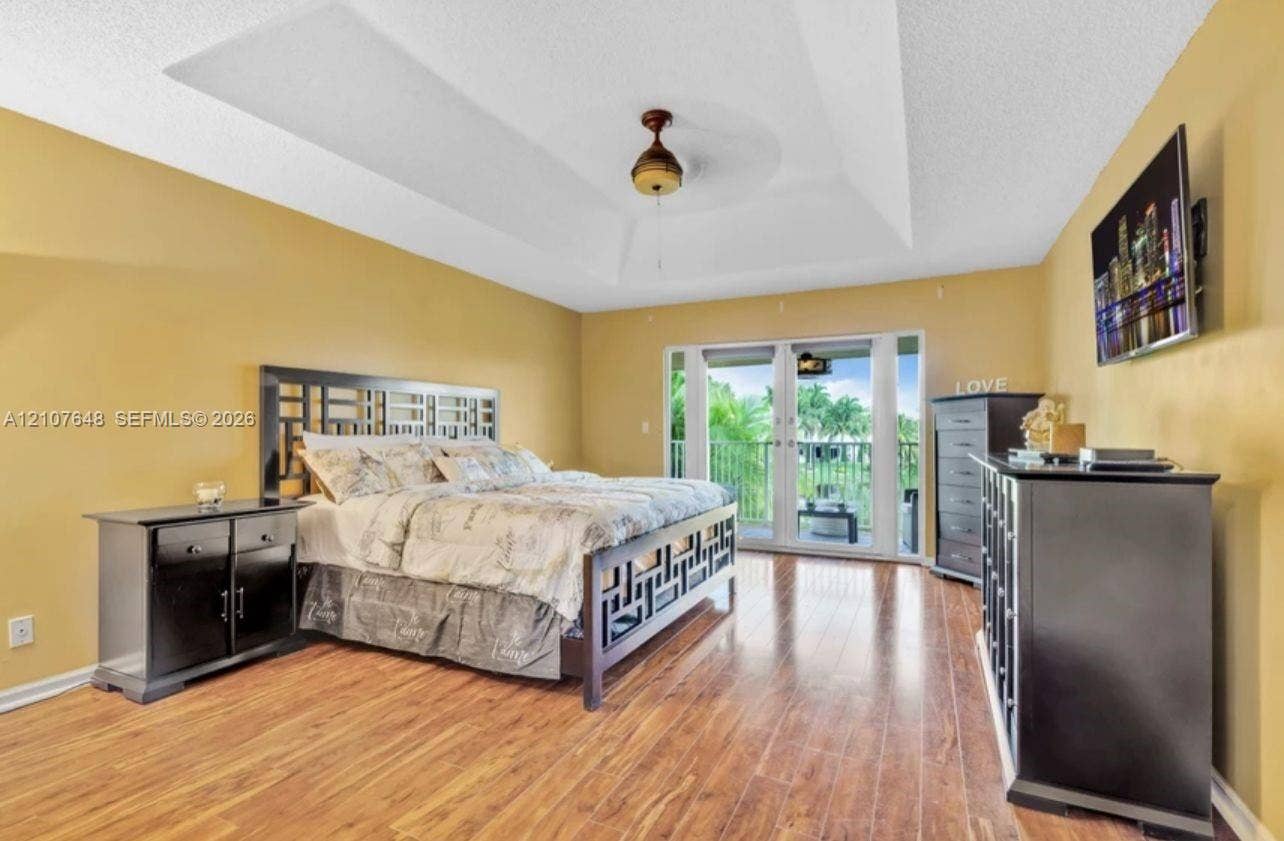 Tray ceiling with central fan, wood-finish flooring, and glass-paned doors opening to a balcony