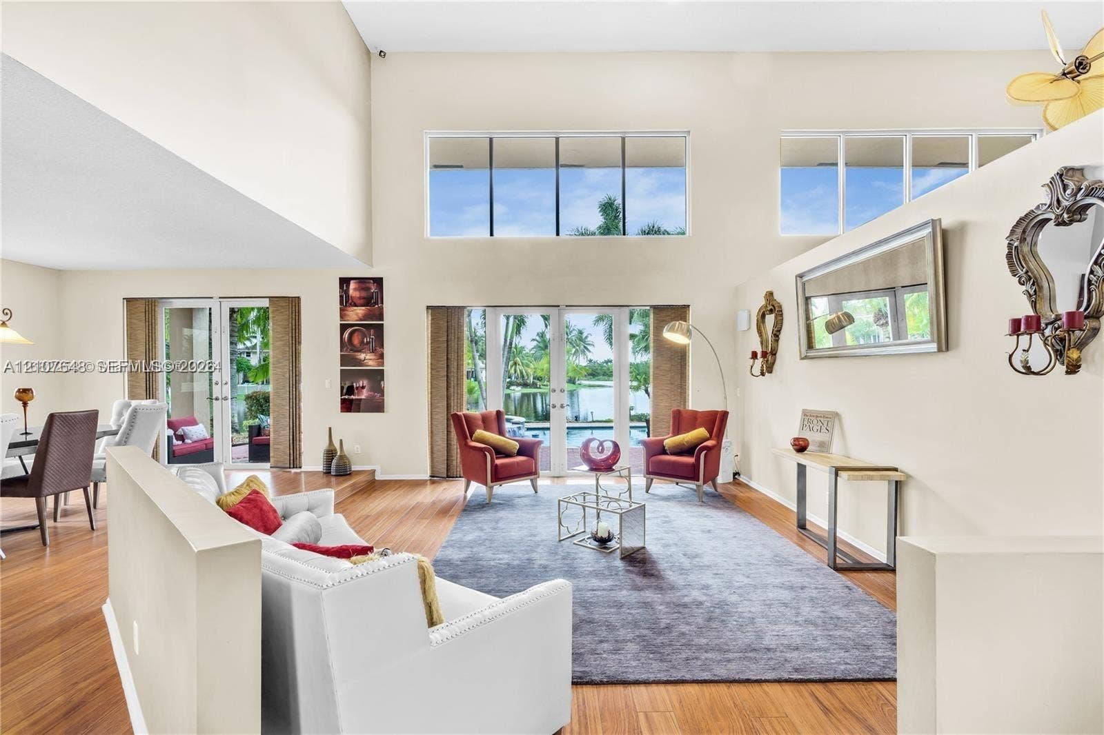 Expansive living area featuring vaulted ceilings, double-height windows, wood-finish flooring, and dual glass-paned doors with exterior water scenery