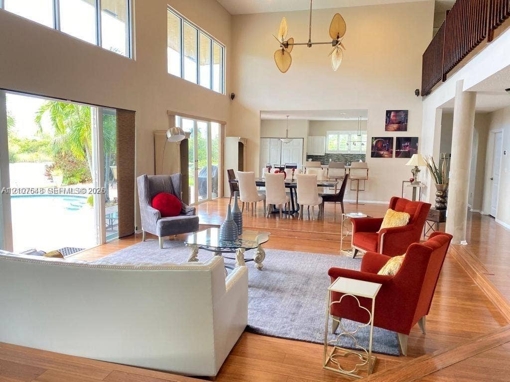 Double-height ceiling with floor-to-ceiling windows, wood-finish flooring, metal multi-arm chandelier, and sliding glass doors