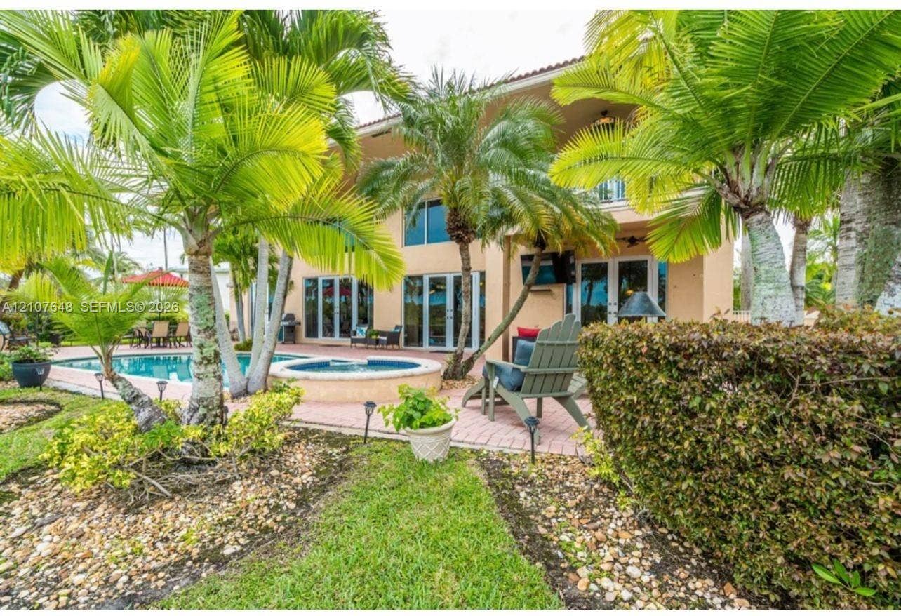 Two-story exterior featuring a swimming pool, integrated spa, paved patio, and mature palm landscaping