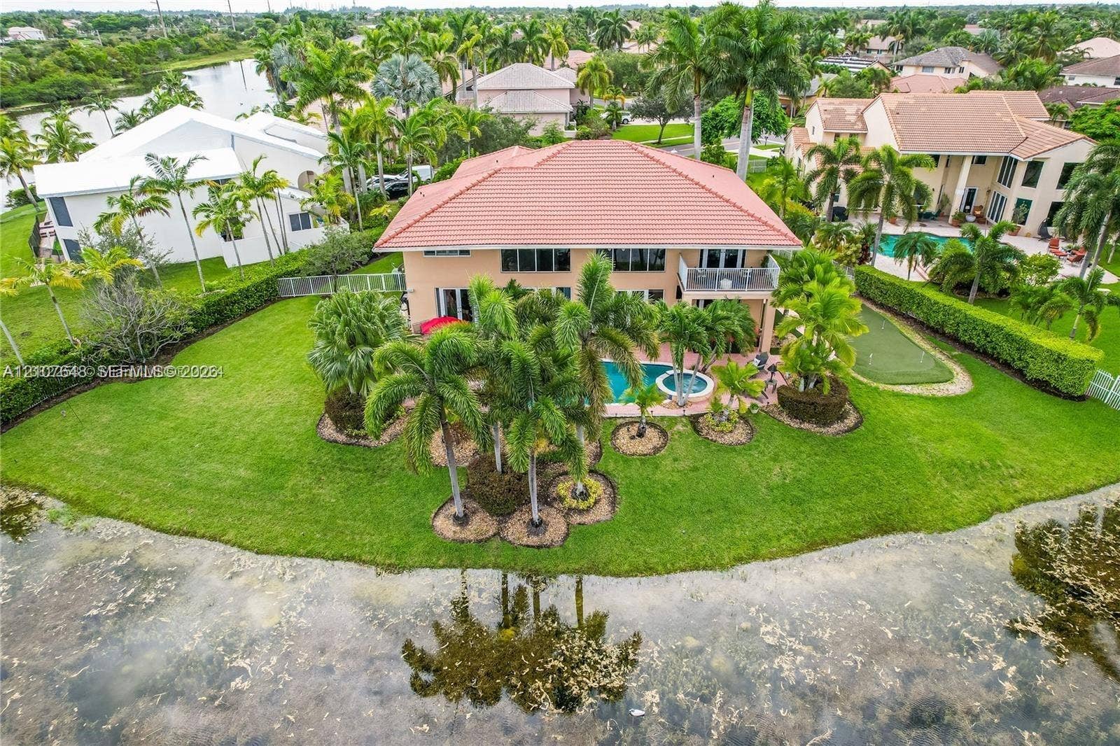 Waterfront residence featuring a tile roof, private swimming pool, built-in putting green, and mature palm landscaping