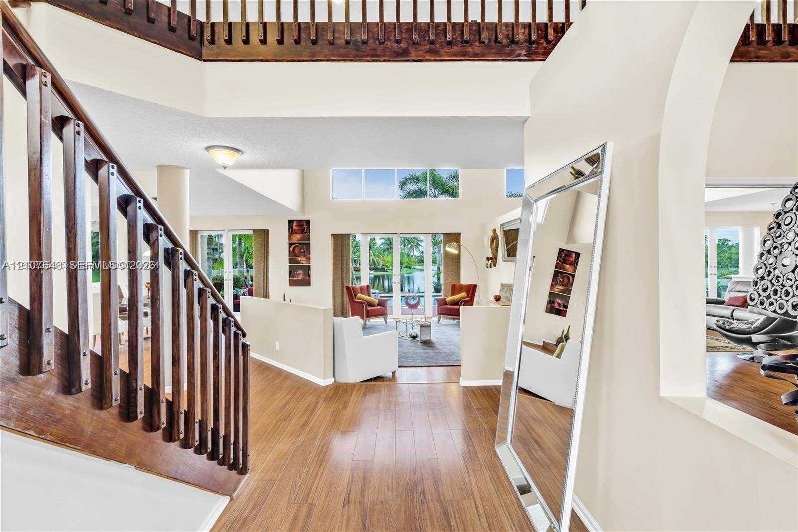 Two-story entryway featuring high ceilings, wood-finish flooring, a wooden staircase with vertical balusters, and arched structural openings