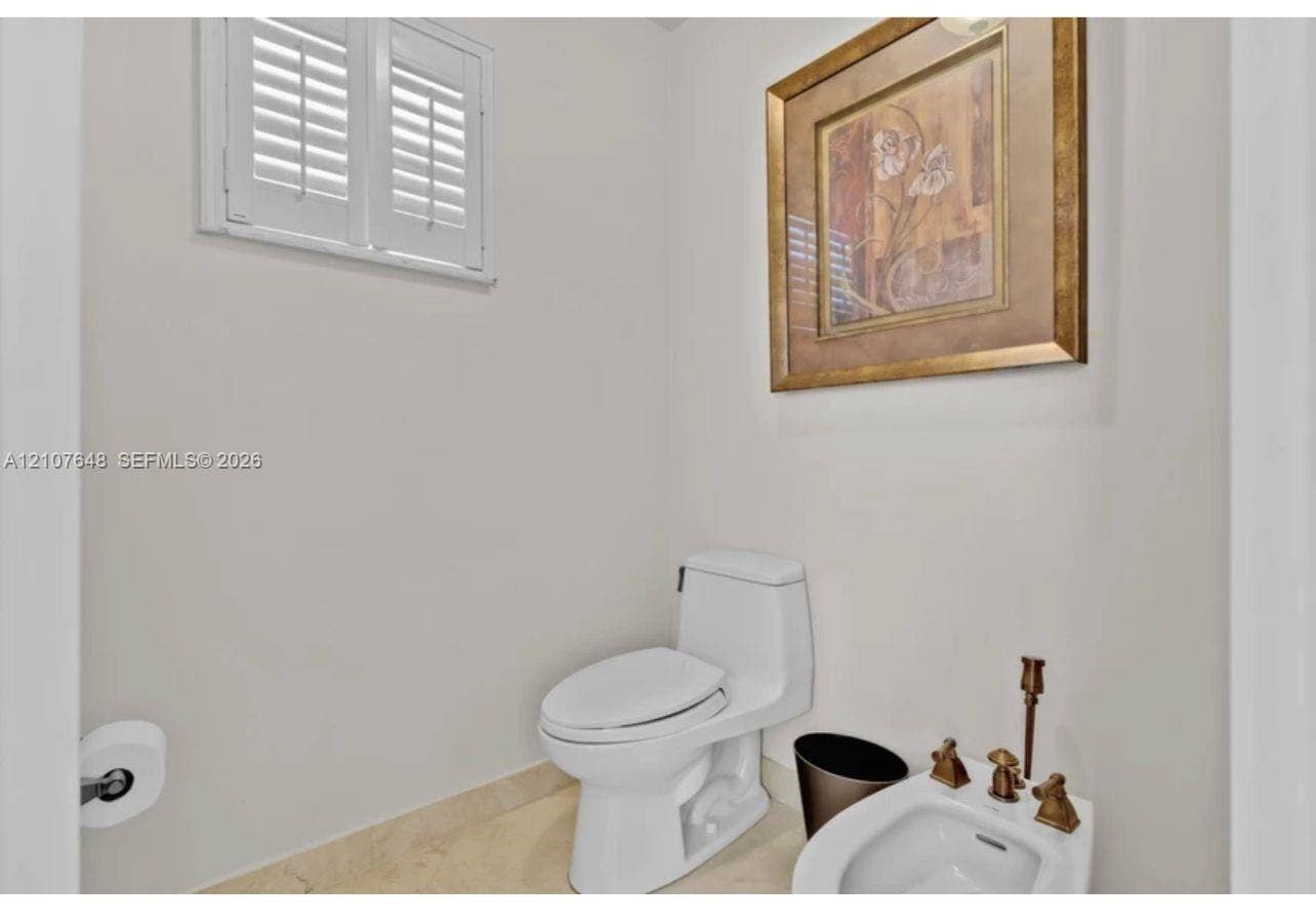 One-piece toilet, bidet with metallic hardware, and white plantation shutters