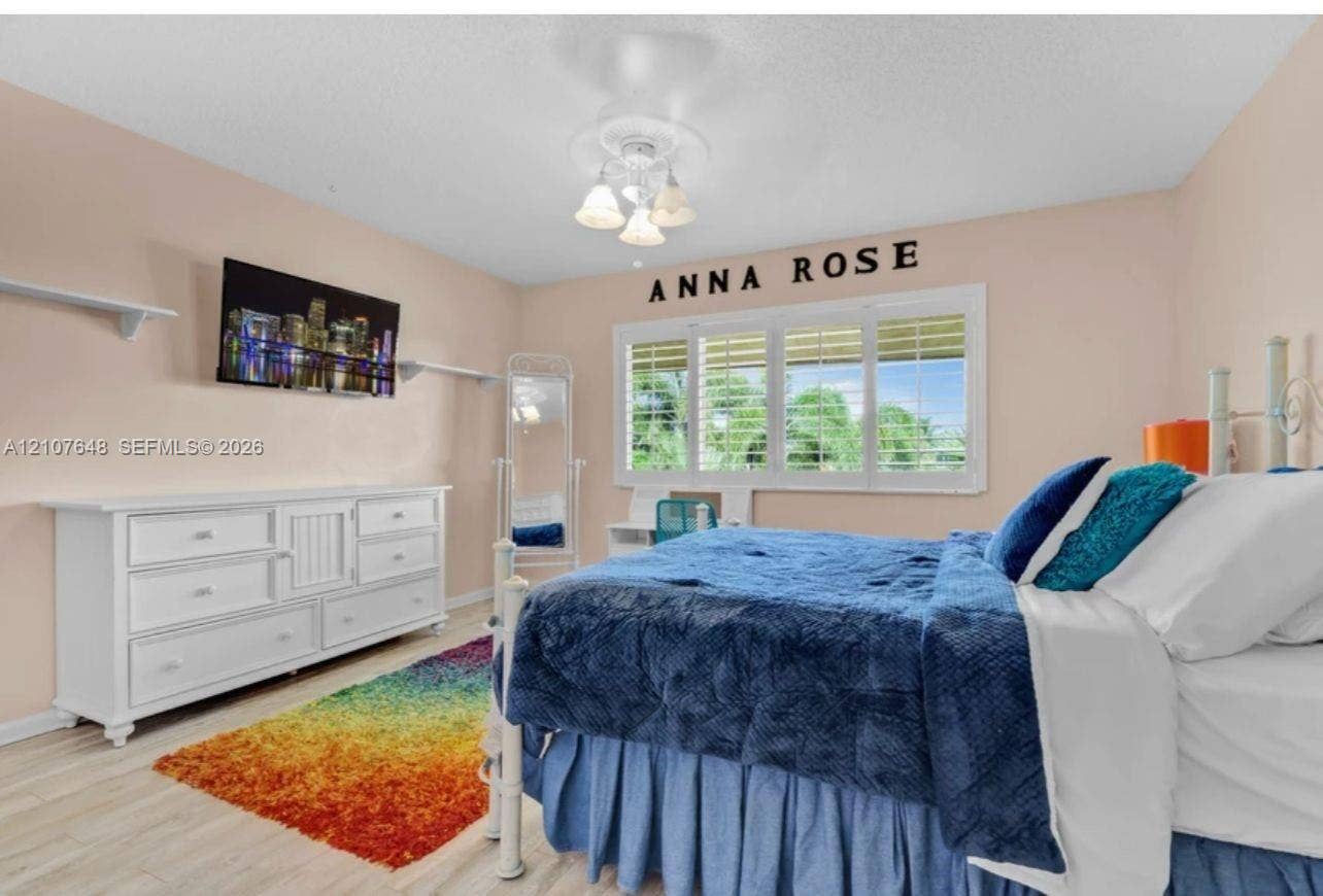Room featuring wood-finish flooring, multi-pane window with interior plantation shutters, and a central ceiling fan with multi-light fixture
