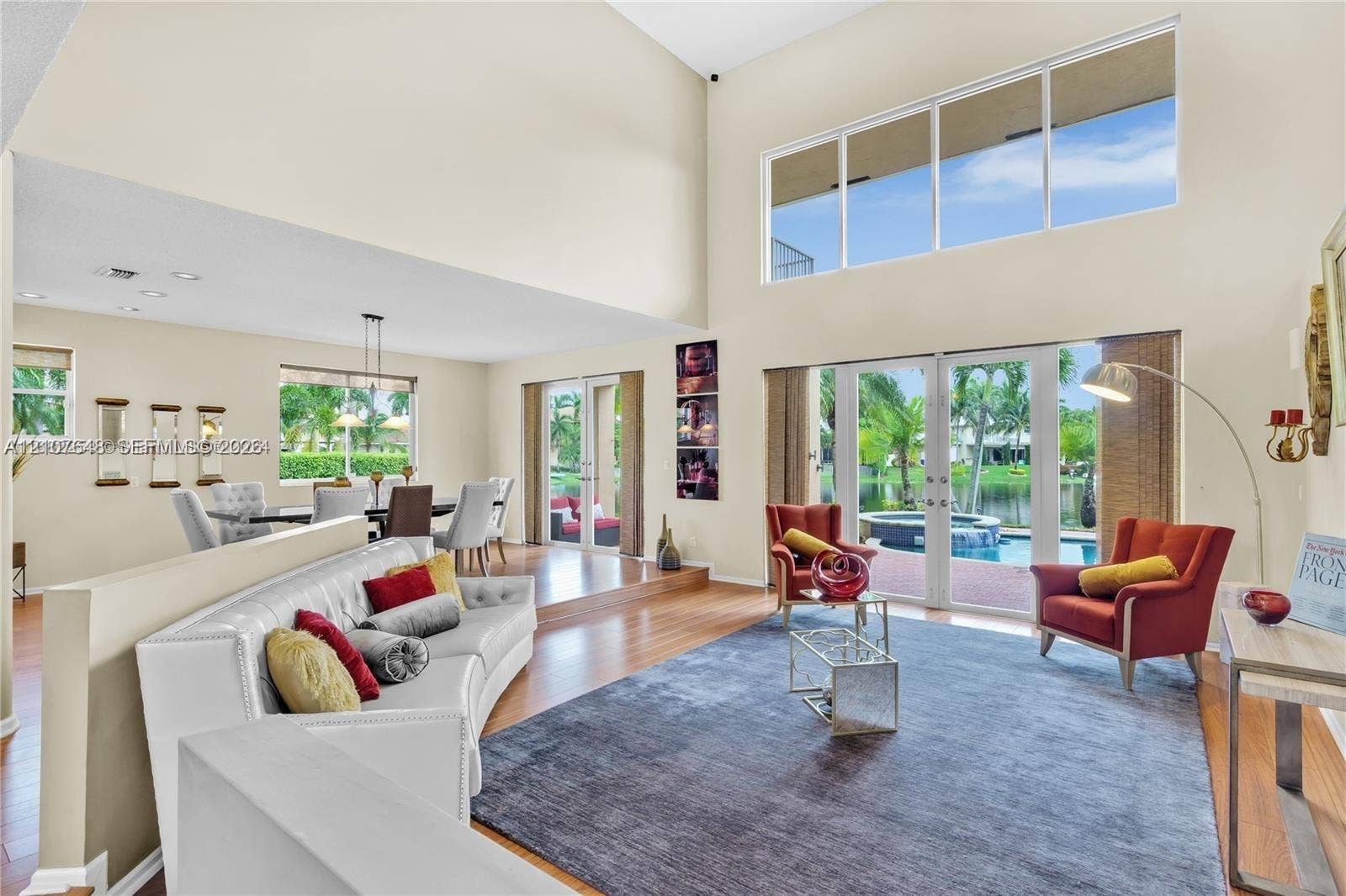 Expansive living area featuring vaulted ceilings, floor-to-ceiling windows, wood-finish flooring, and glass double doors opening to a pool and spa