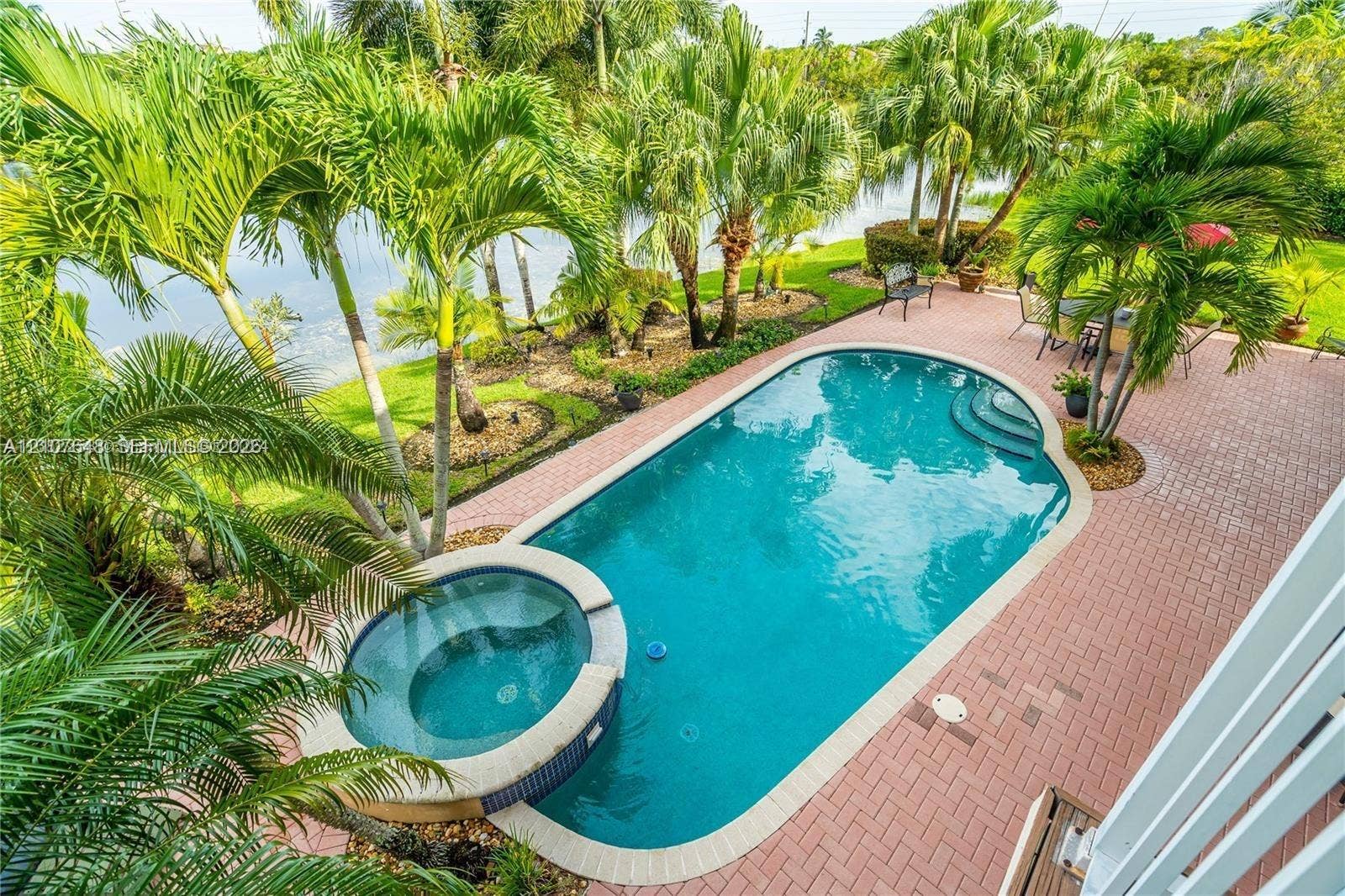 In-ground pool with integrated spillover spa, brick paver patio, lush landscaping, and water frontage