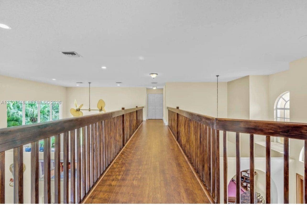 Elevated walkway featuring wood-finish flooring, full-length dark-stained wooden railings, recessed lighting, and arched window detailing