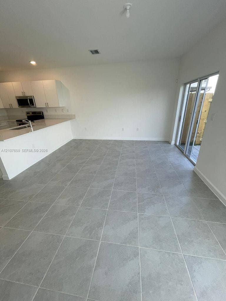 1787 SE 26th Terrace, Homestead, Homestead, FL 33035 Kitchen featuring white cabinetry, quartz-surface countertops, and built-in stainless steel appliances, complemented by large-format gray tile flooring and sliding glass doors