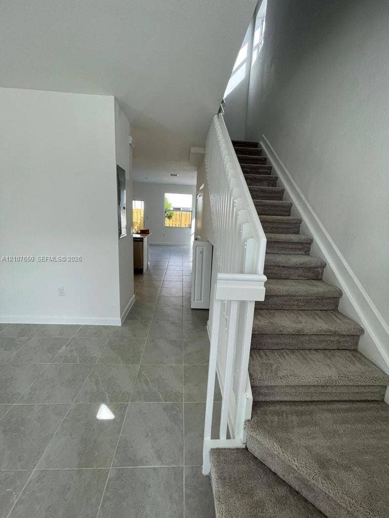 1787 SE 26th Terrace, Homestead, Homestead, FL 33035 Neutral-toned tile flooring, carpeted staircase with white painted wood balusters, and minimalist wall finishes