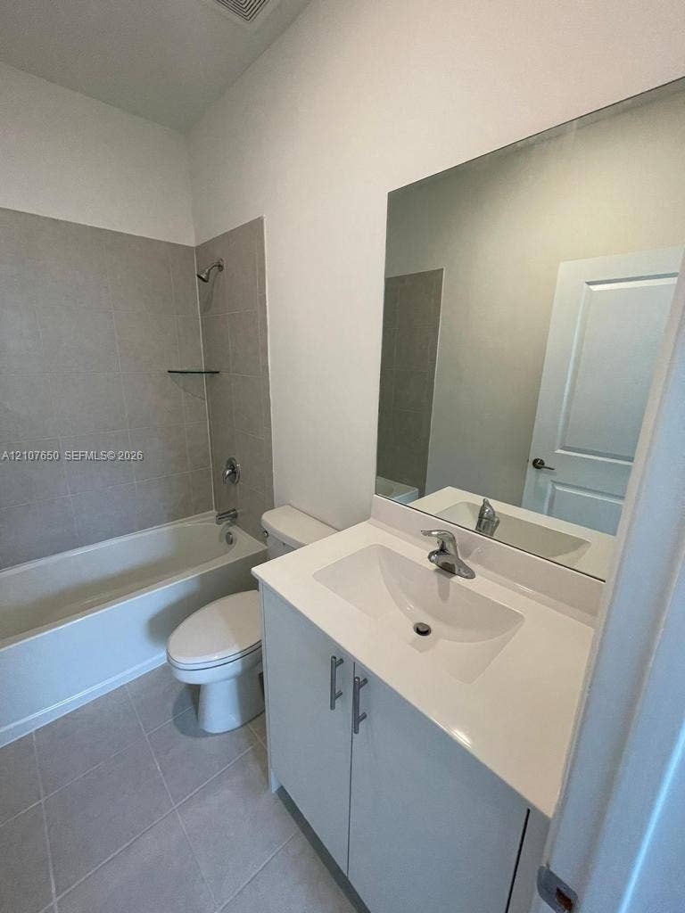 1787 SE 26th Terrace, Homestead, Homestead, FL 33035 Bathroom featuring a vanity with a white countertop and integrated sink, full-width wall mirror, tile-surround bathtub, and neutral ceramic floor tiling