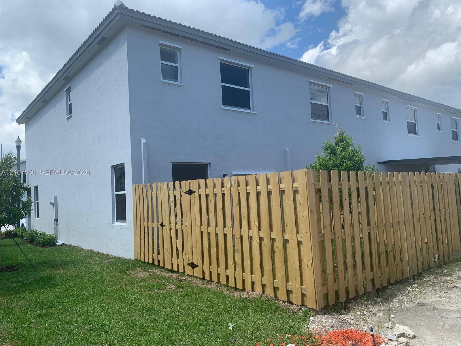 1787 SE 26th Terrace, Homestead, Homestead, FL 33035 Two-story exterior with a light-toned stucco finish, multiple single-hung windows, and a wood-slat privacy fence enclosing a grass lawn