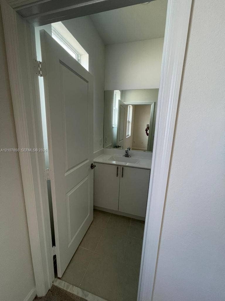 1787 SE 26th Terrace, Homestead, Homestead, FL 33035 White vanity cabinet with an integrated rectangular basin, single-handle chrome faucet, large rectangular wall mirror, and neutral tile flooring