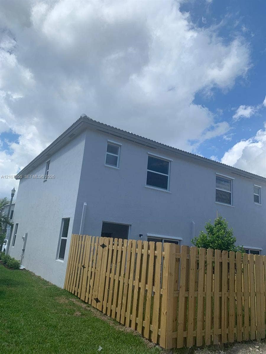 1787 SE 26th Terrace, Homestead, Homestead, FL 33035 Two-story exterior featuring a light-toned stucco facade, neutral-hued tiled roof, multiple rectangular windows, and a wood-slat privacy fence