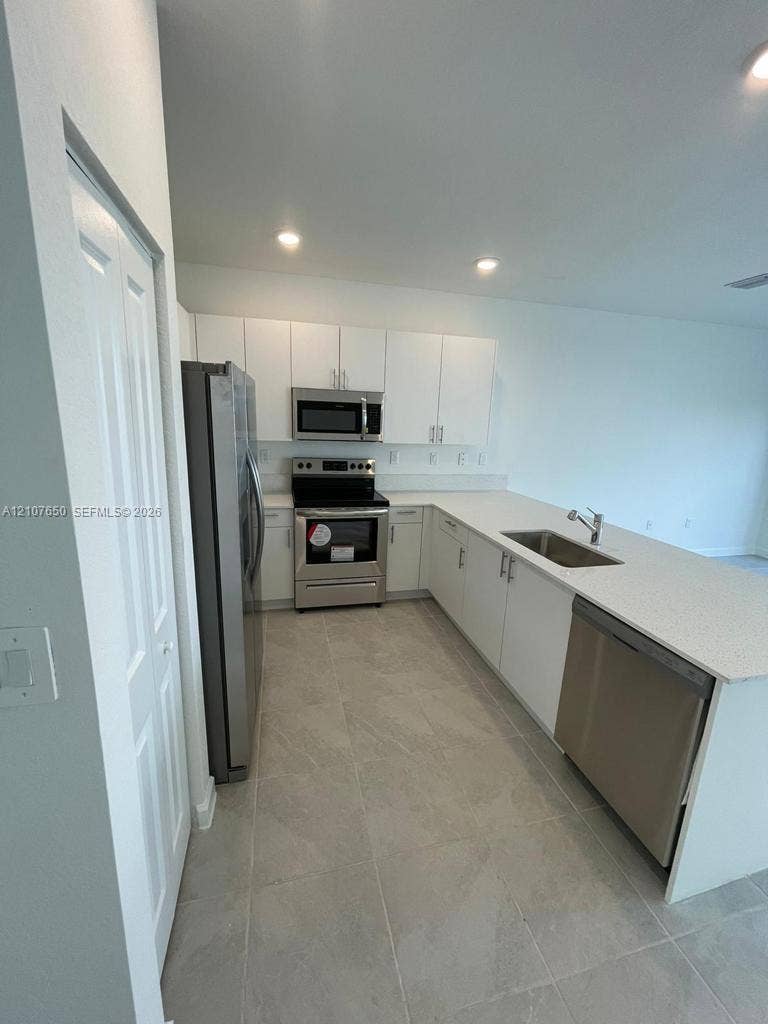 1787 SE 26th Terrace, Homestead, Homestead, FL 33035 Kitchen featuring white cabinetry, solid-surface countertops, stainless steel appliances, a center island with an undermount sink, and tile flooring
