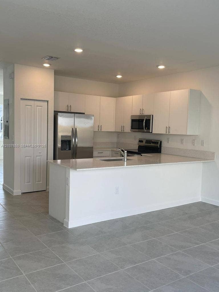 1787 SE 26th Terrace, Homestead, Homestead, FL 33035 Kitchen featuring white flat-panel cabinetry, a stainless steel refrigerator and microwave, a peninsula with stone-surface countertops, and gray tile flooring