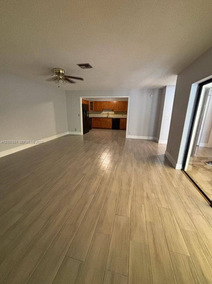 Wood-finish tile flooring, ceiling fan with integrated lighting, and kitchen featuring wood cabinetry and dark-toned appliances