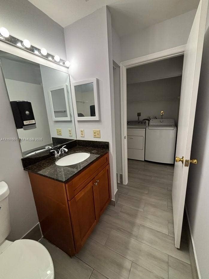 Bathroom featuring a wood-finish vanity with a stone-surround countertop, integrated porcelain sink, full-width vanity mirror, and linear vanity lighting, complemented by tile flooring
